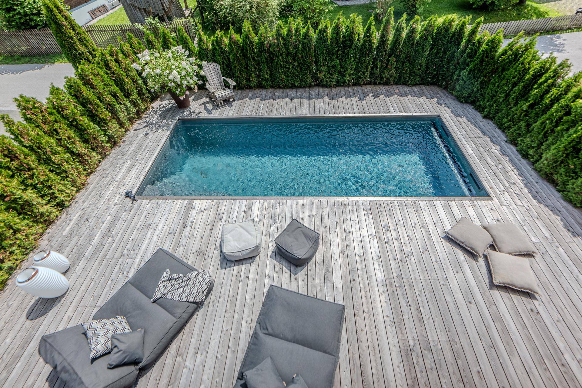 Übersicht des Außenbereichs mit langem Pool und großzügiger Holzterrasse, umgeben von grünen Hecken.