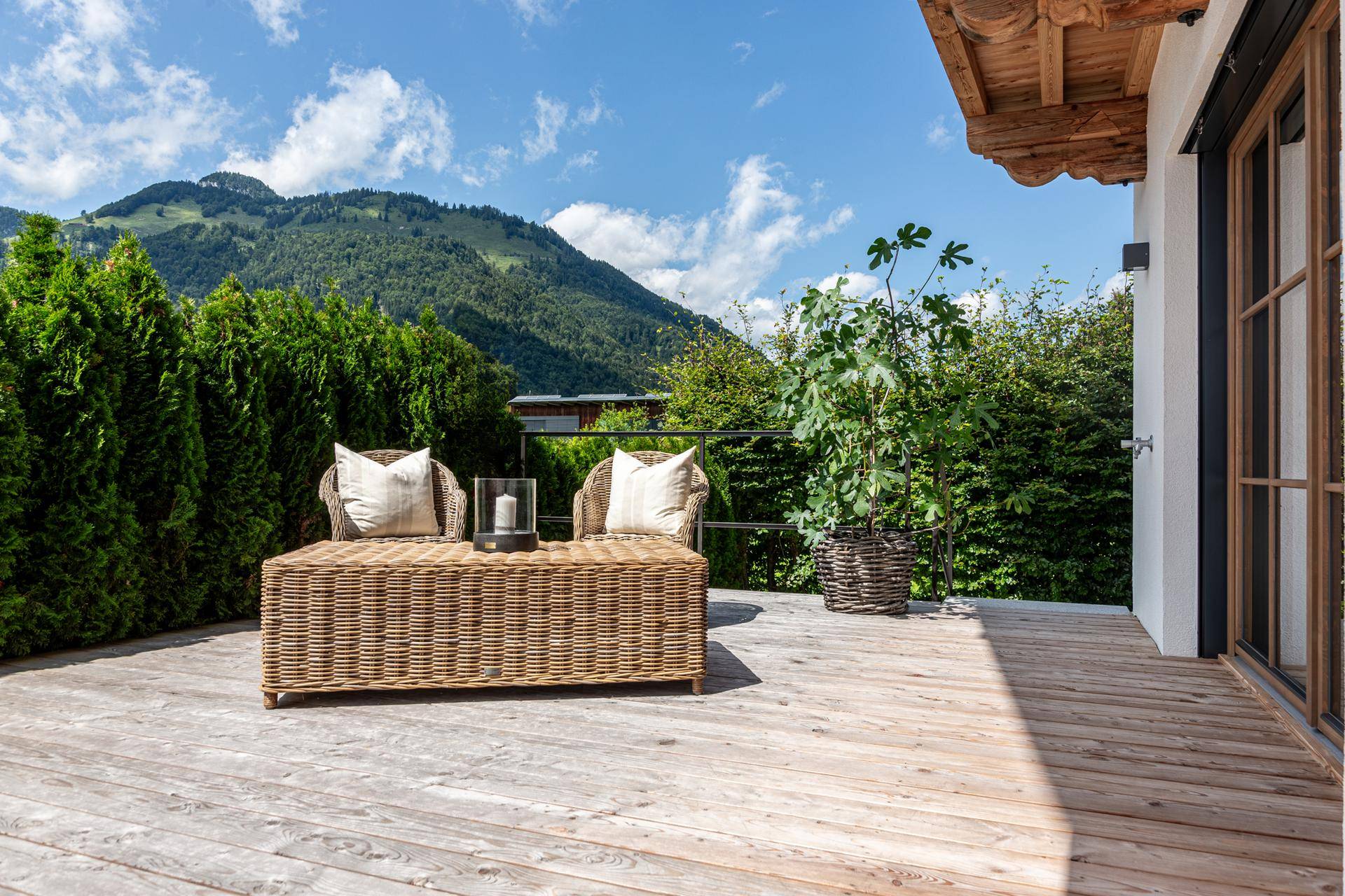 Eine weitere Holzterrasse mit Korbmöbeln bietet einen idyllischen Sitzbereich mit Bergblick.