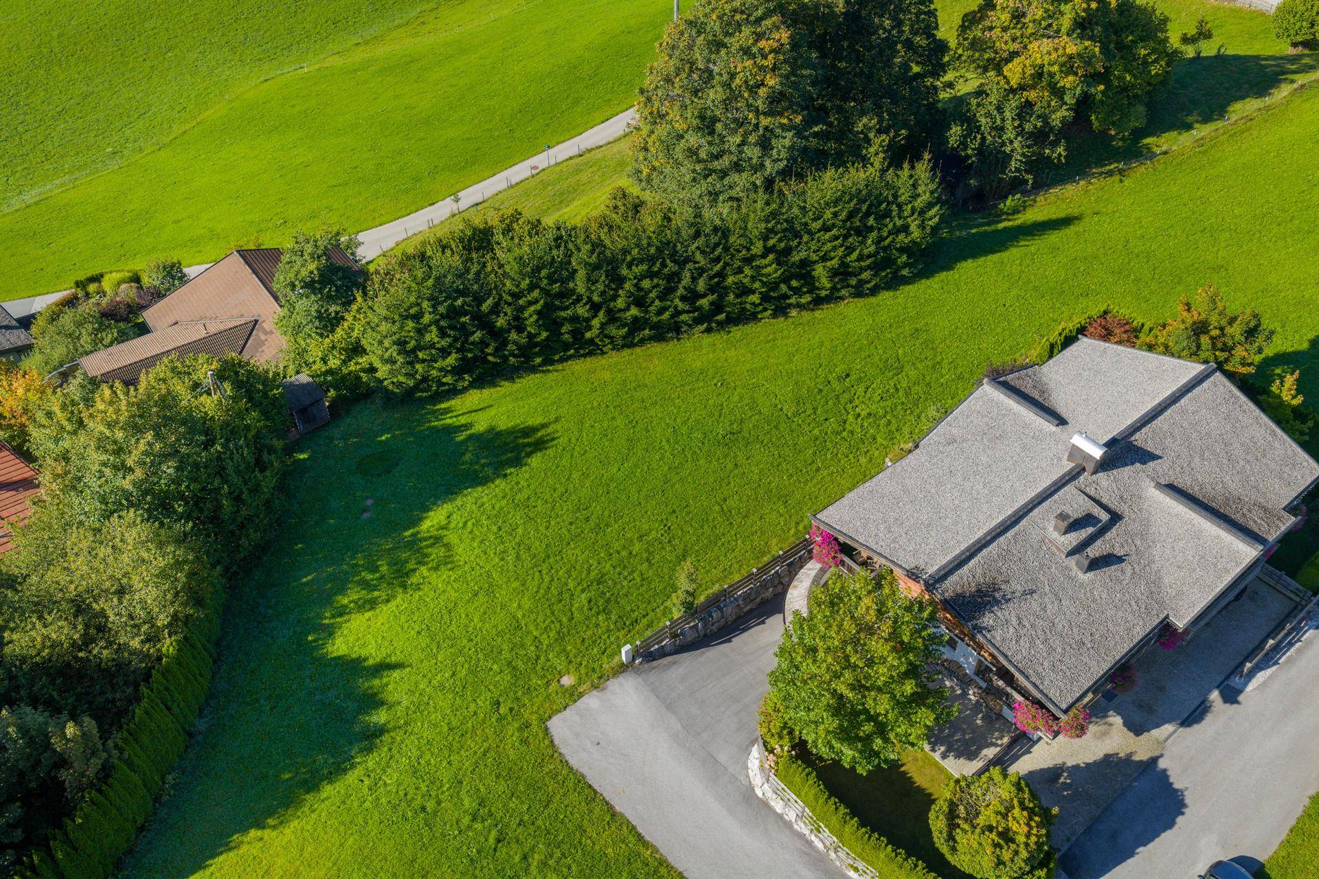 Draufsicht auf das Haus mit traditionellem Dach und weitläufigen grünen Flächen in sonniger Umgebung.
