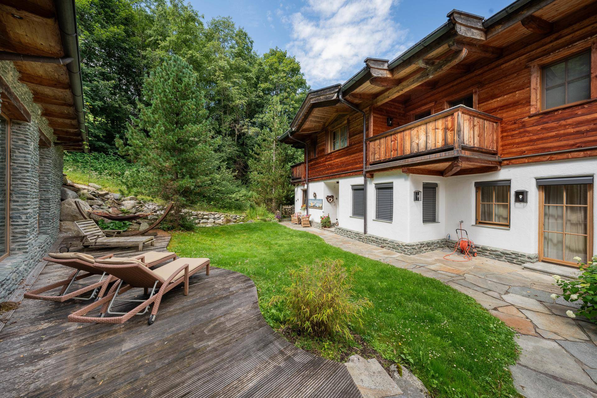 Außenbereich mit Holzterrasse, Liegestühlen und weitläufigem Rasen vor der Chalet-Fassade.