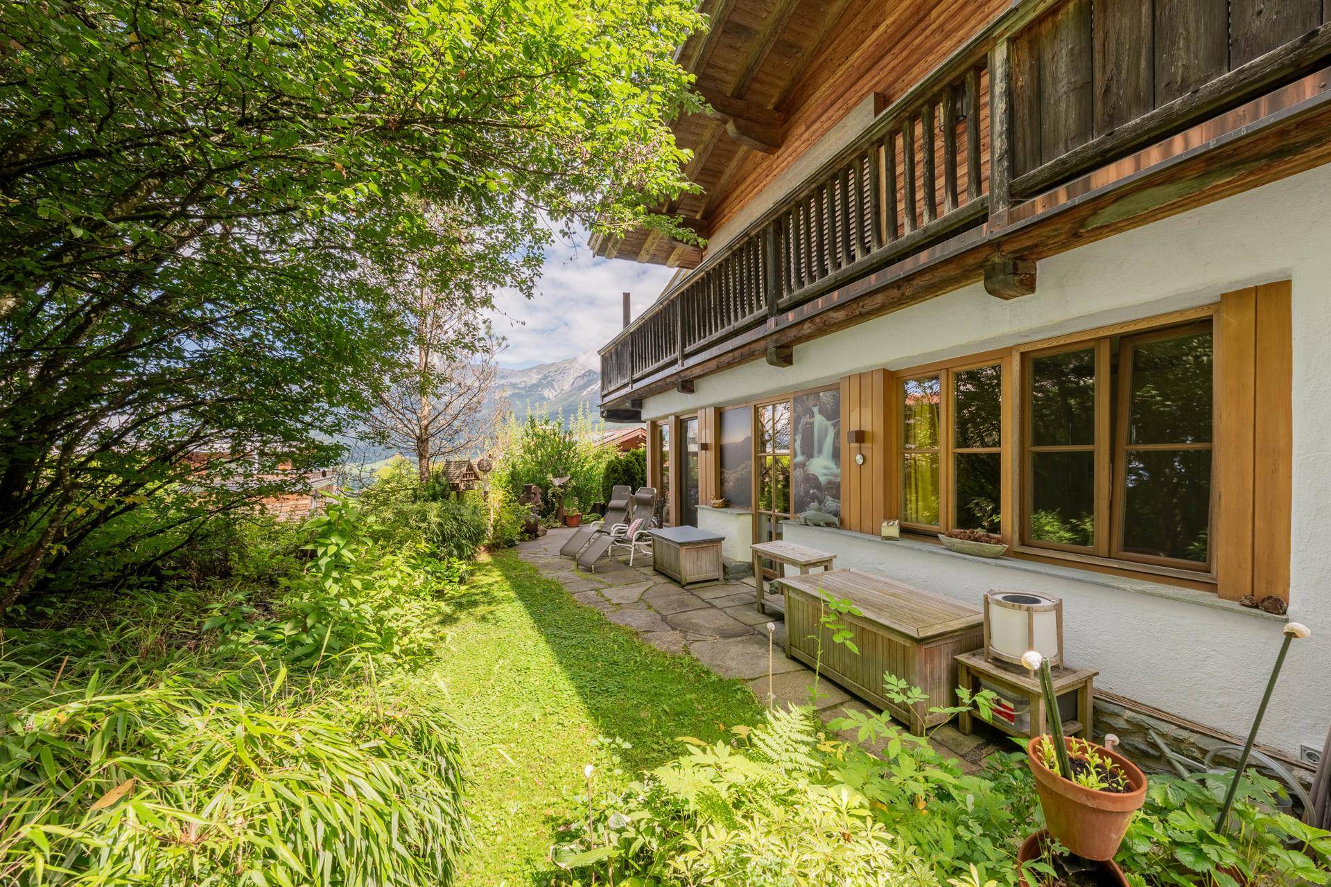 Idyllischer Gartenbereich mit Terrasse, üppiger Vegetation und Blick auf die umliegende Berglandschaft.