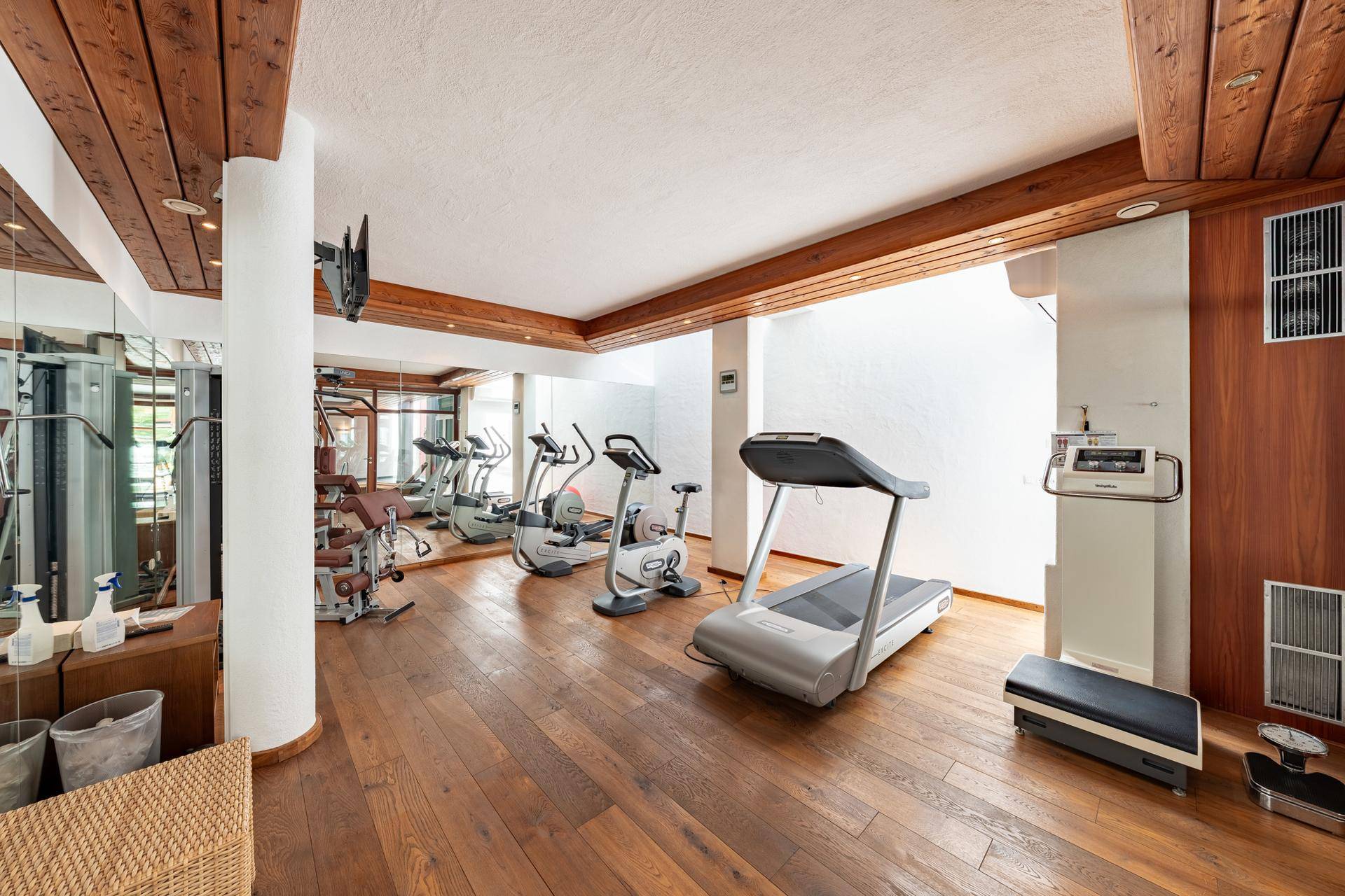 Gut ausgestatteter Fitnessraum mit verschiedenen Trainingsgeräten und Holzfußboden.
