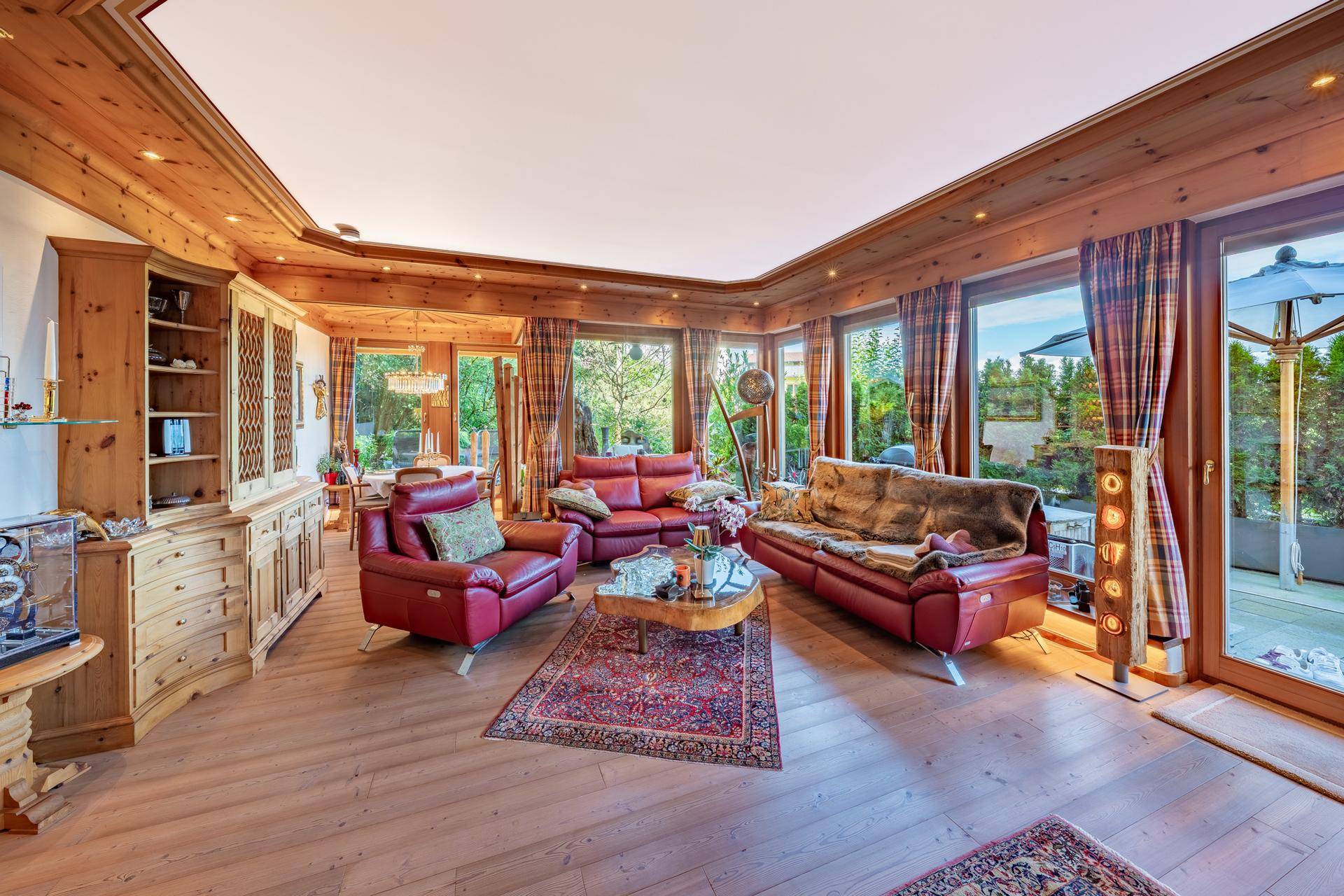 Geräumiges Wohnzimmer im alpinen Stil mit Holzelementen, roten Ledersofas und großen Fenstern.