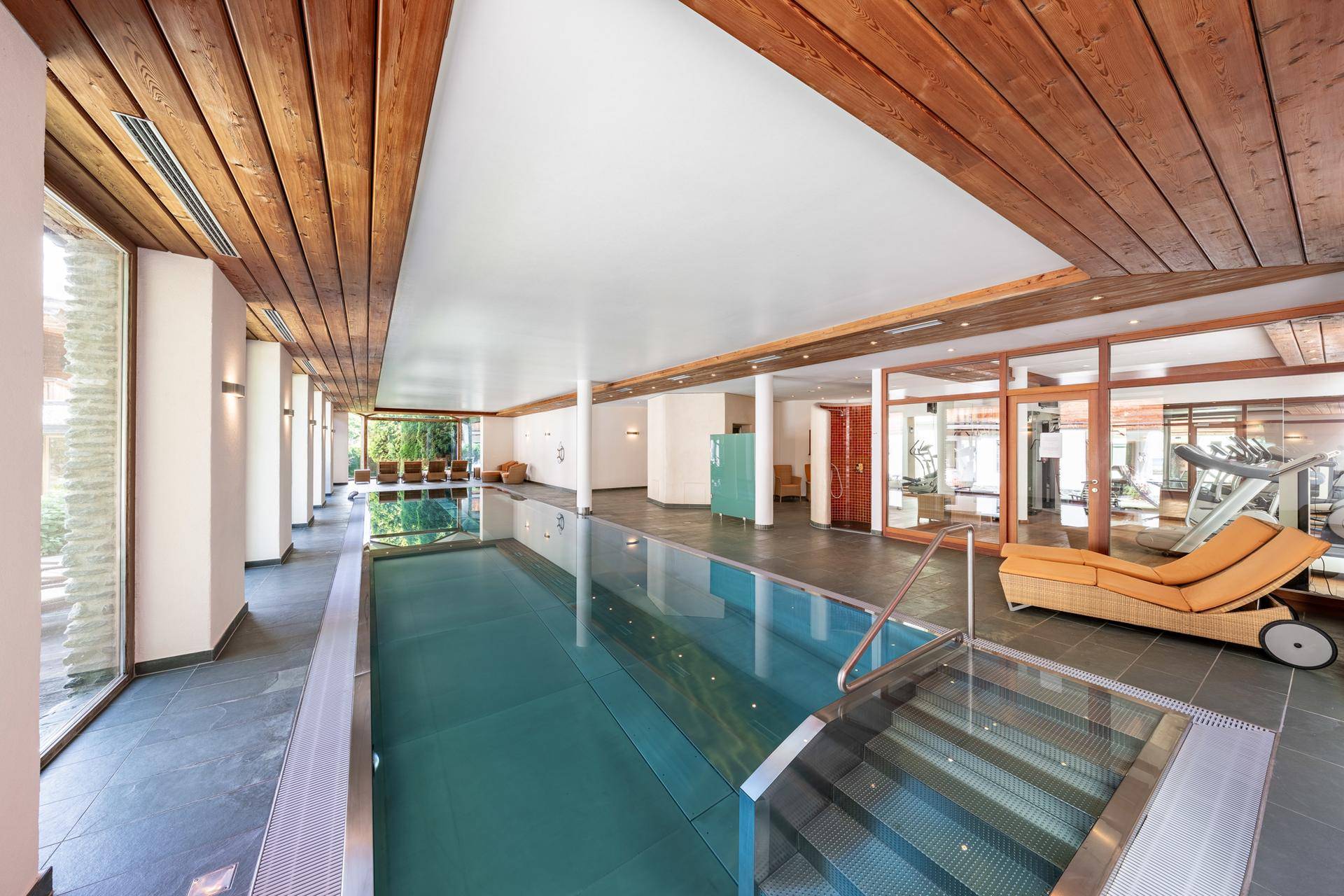 Exklusiver Innenpoolbereich mit Holzdecken und angrenzendem Fitnessraum für Wellness.