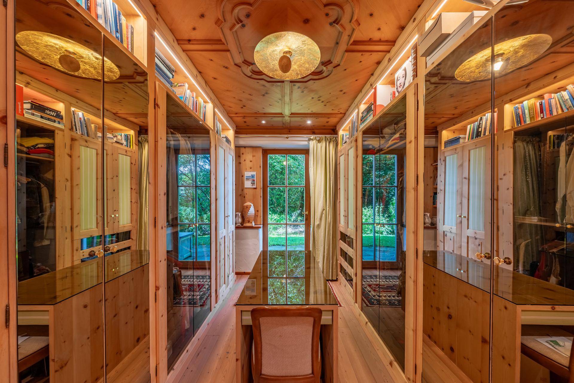 Begehbarer Kleiderschrank mit Holzvertäfelung, Spiegeltüren und integrierten Bücherregalen.
