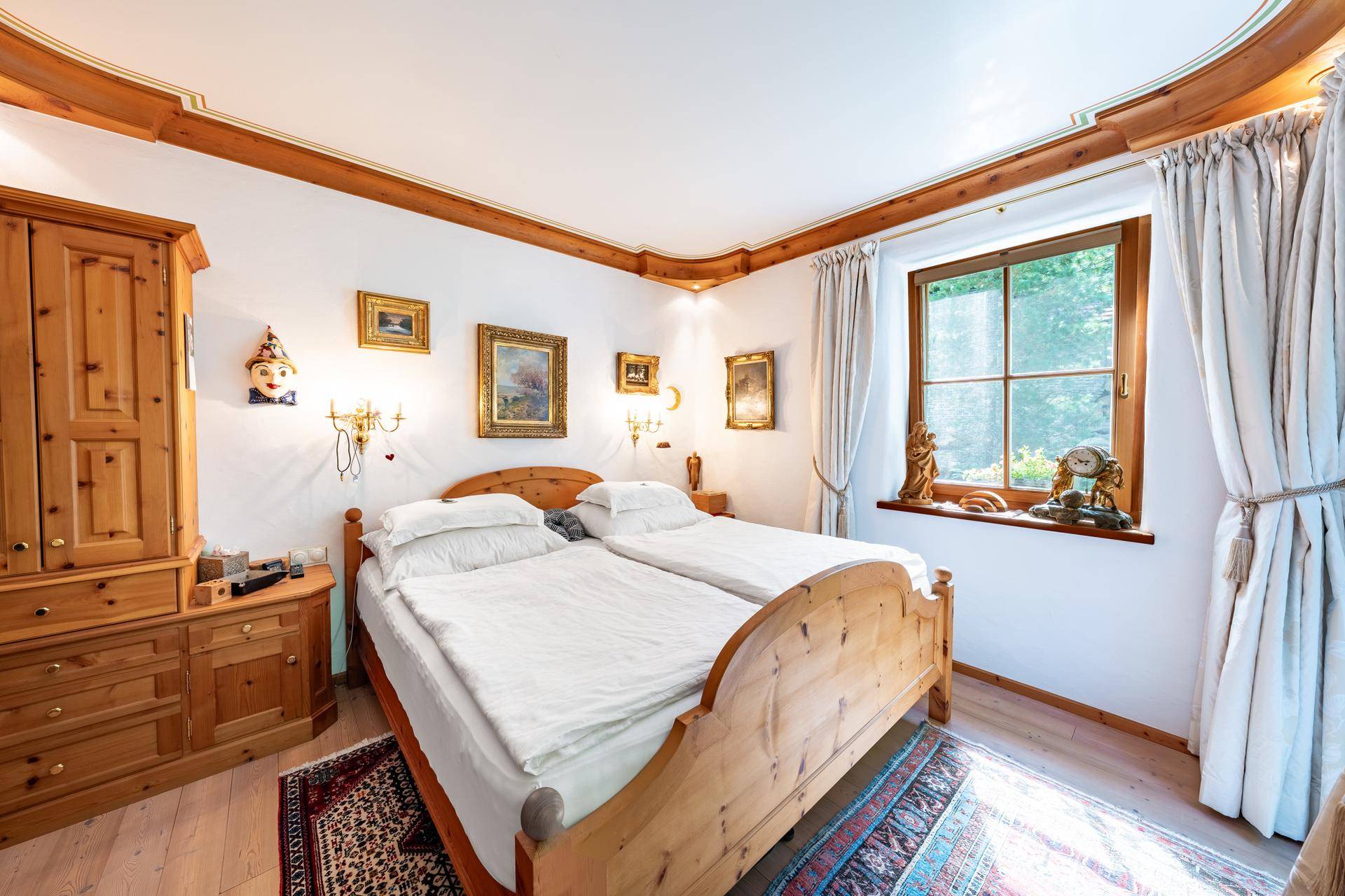 Gemütliches Schlafzimmer mit traditionellen Holzmöbeln, Doppelbett und Fenster mit Grünblick.