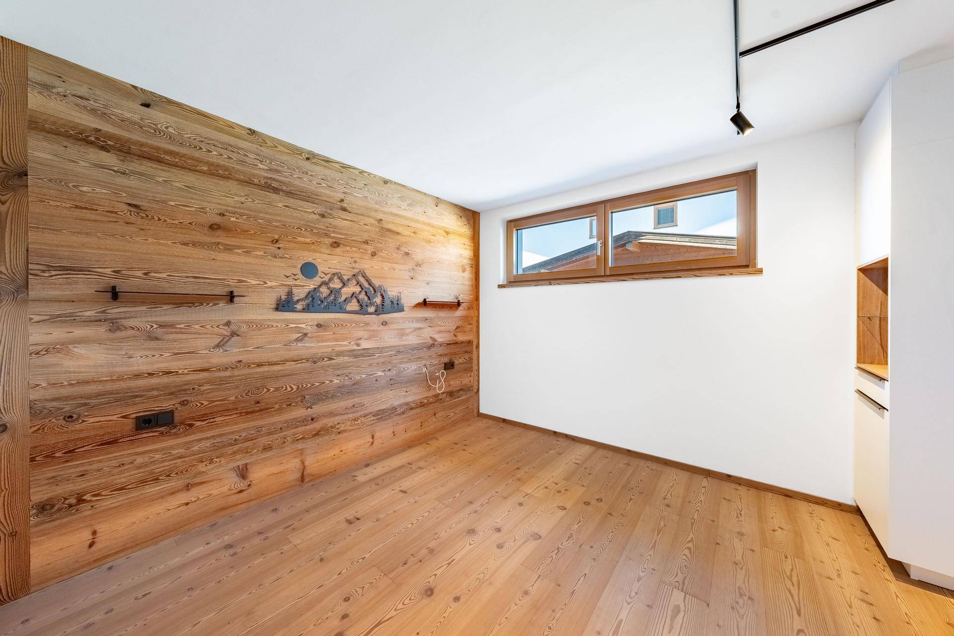 Heller Raum mit einer Holzakzentwand, Holzboden und einem Fenster, das Tageslicht hereinlässt.