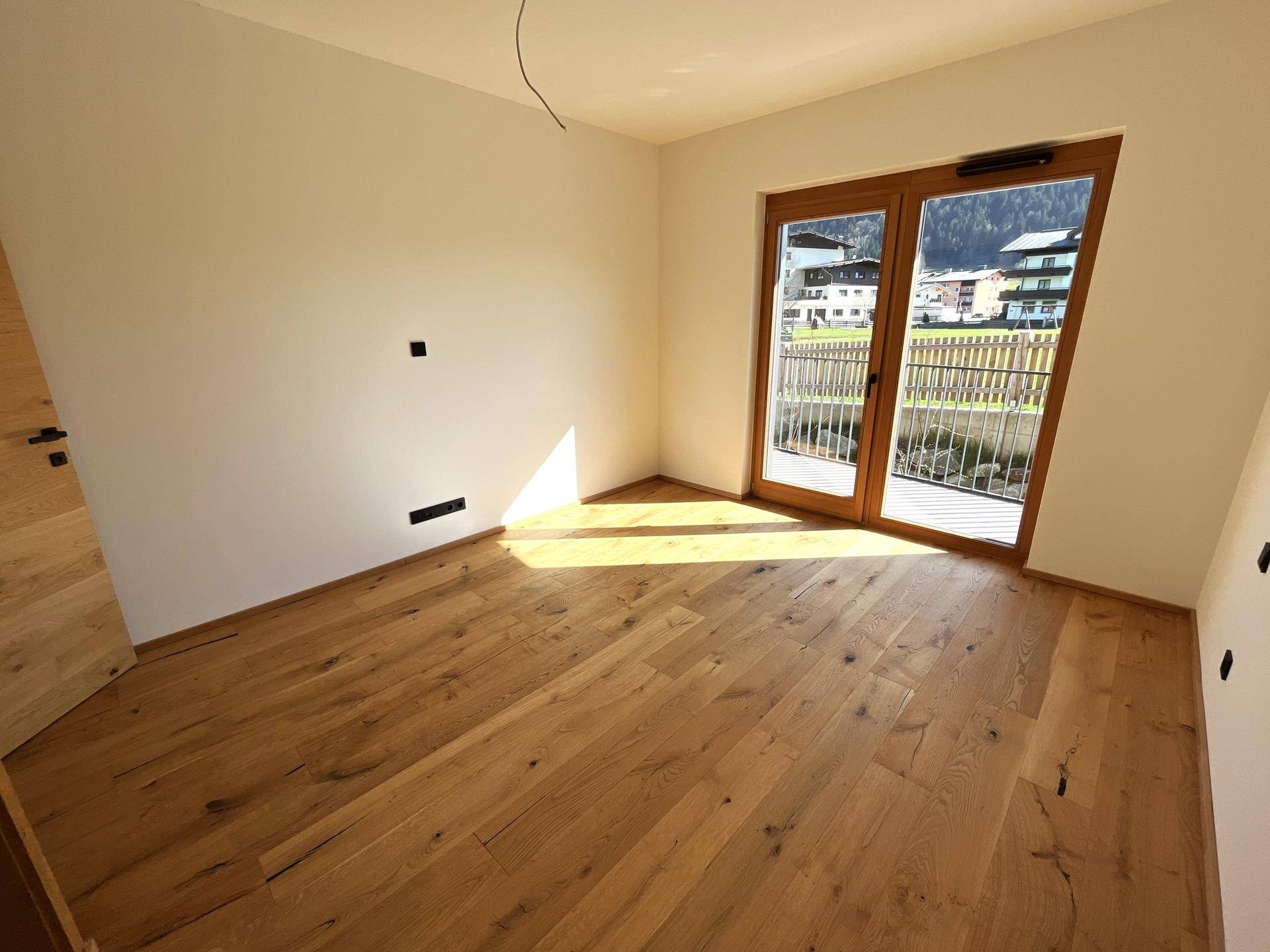 Lichtdurchflutetes Schlafzimmer mit Holzboden und großem Fenster mit Bergblick und Balkonzugang.