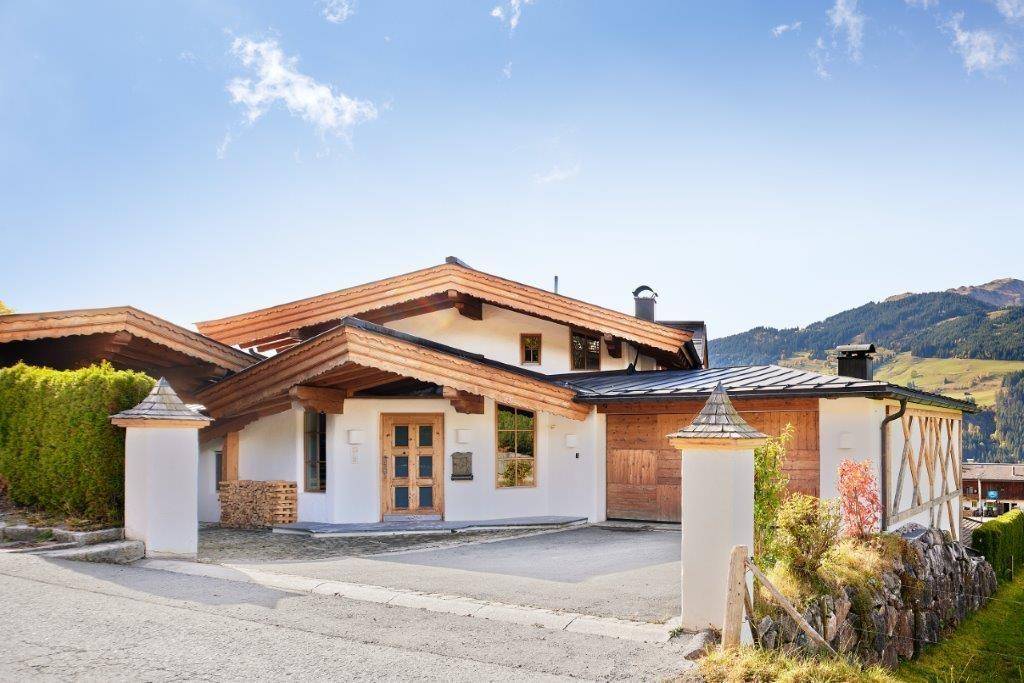 Charmantes Alpenhaus mit Holzdach und weißer Fassade, umgeben von gepflegter Landschaftsgestaltung.