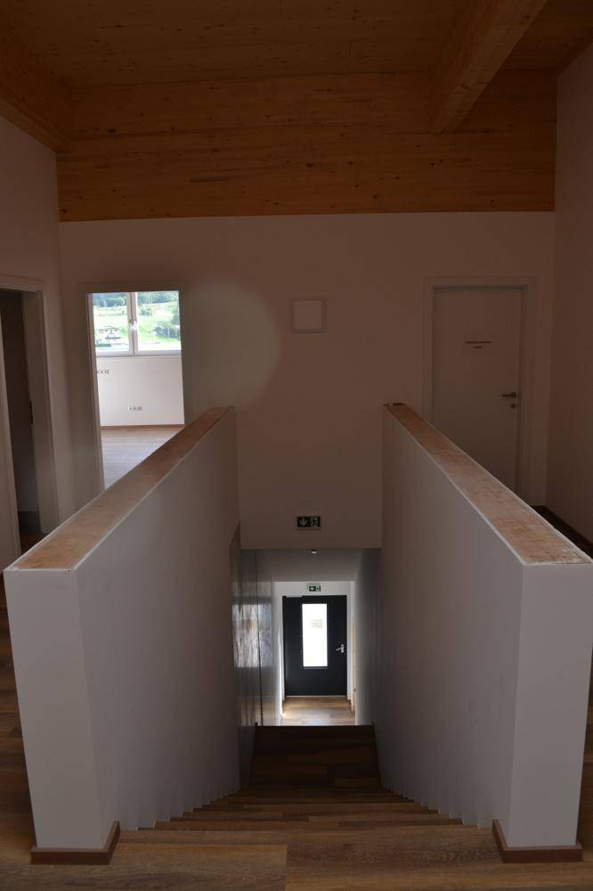 Blick von oben auf eine Holztreppe mit weißen Brüstungen und einer Holzbalkendecke.
