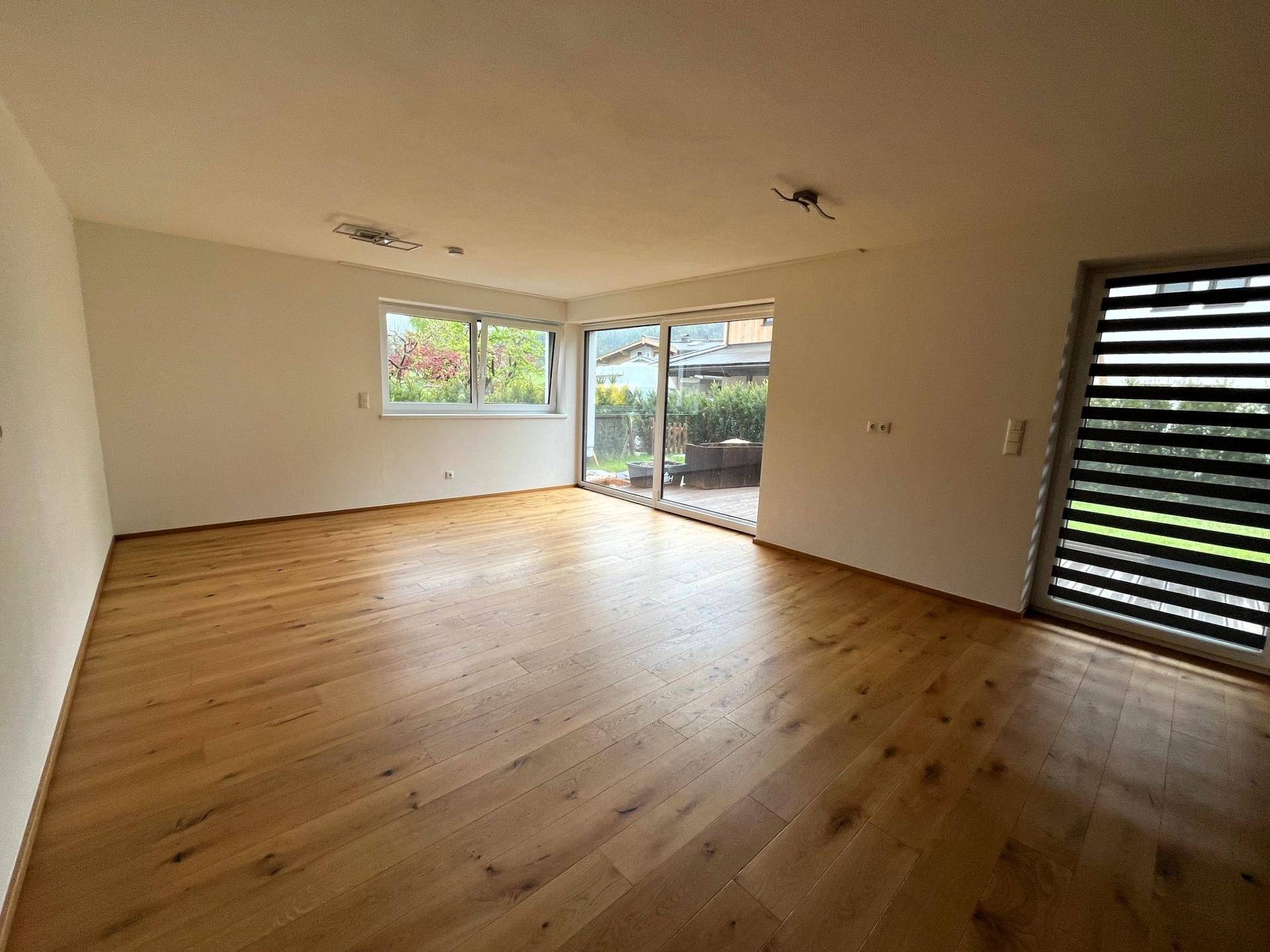 Heller Wohnbereich mit Holzboden und großen Fenstern, die viel Tageslicht hereinlassen.