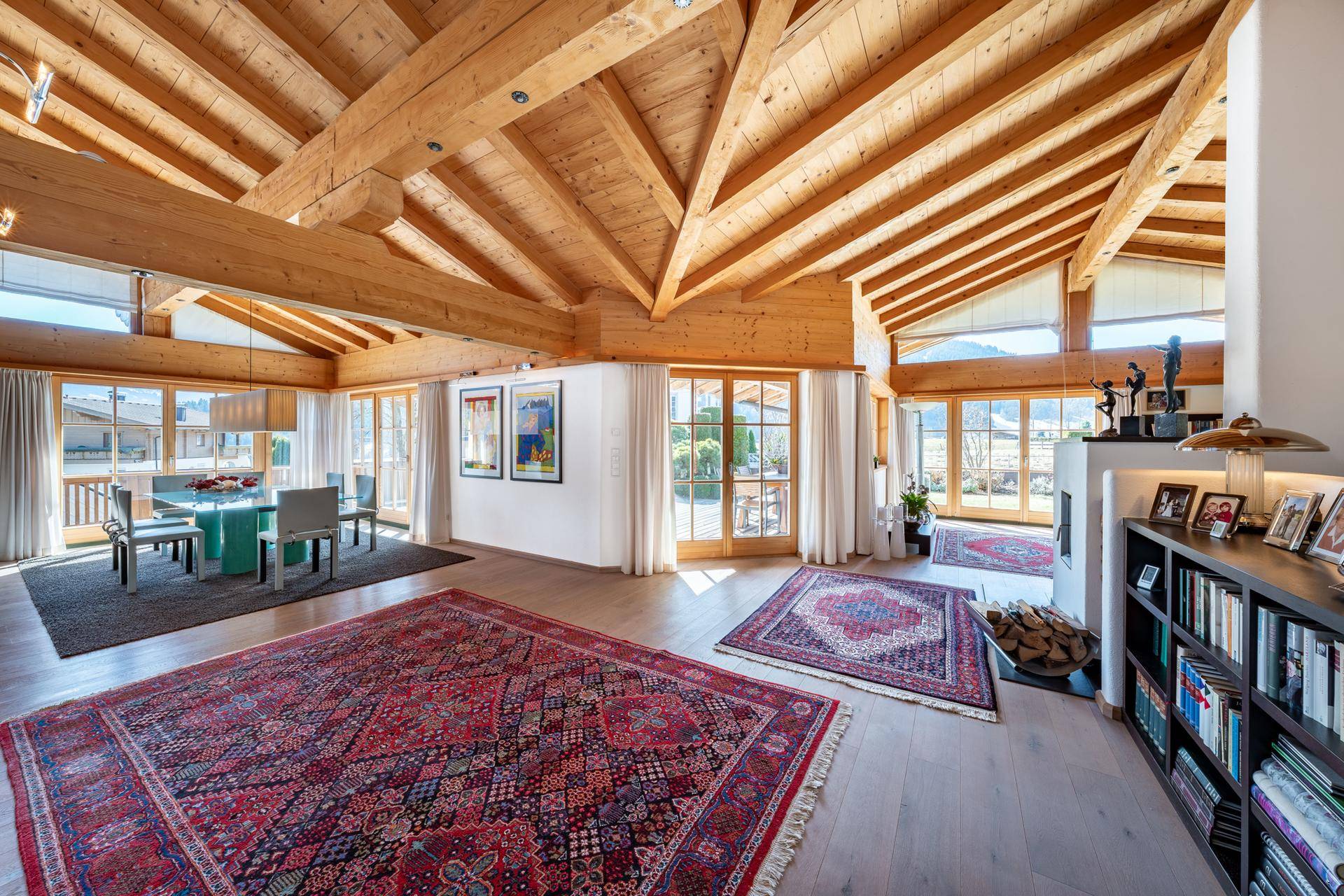Lichtdurchfluteter Wohn- und Essbereich mit hohen Holzdecken, Holzbalken und großen Fenstern.