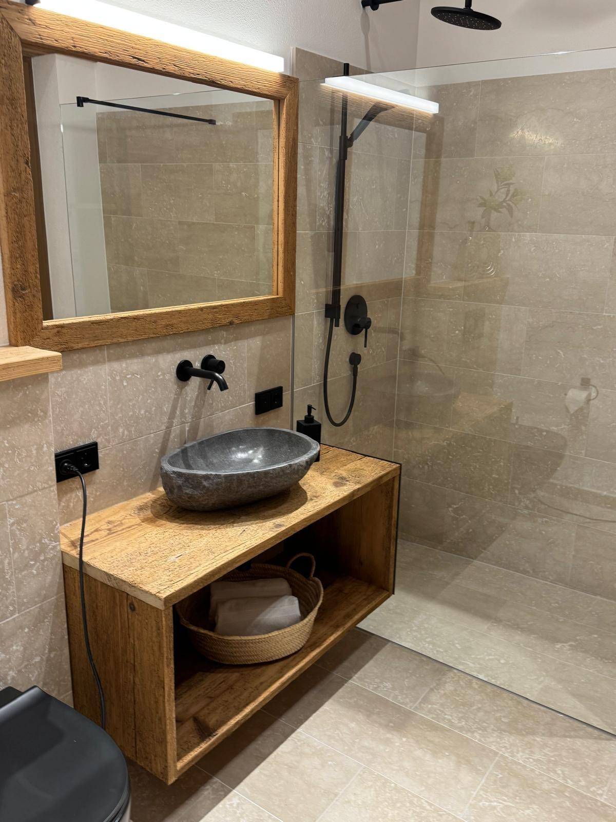 Modernes Badezimmer mit Natursteinwaschbecken, Holzwaschtisch und begehbarer Regendusche.