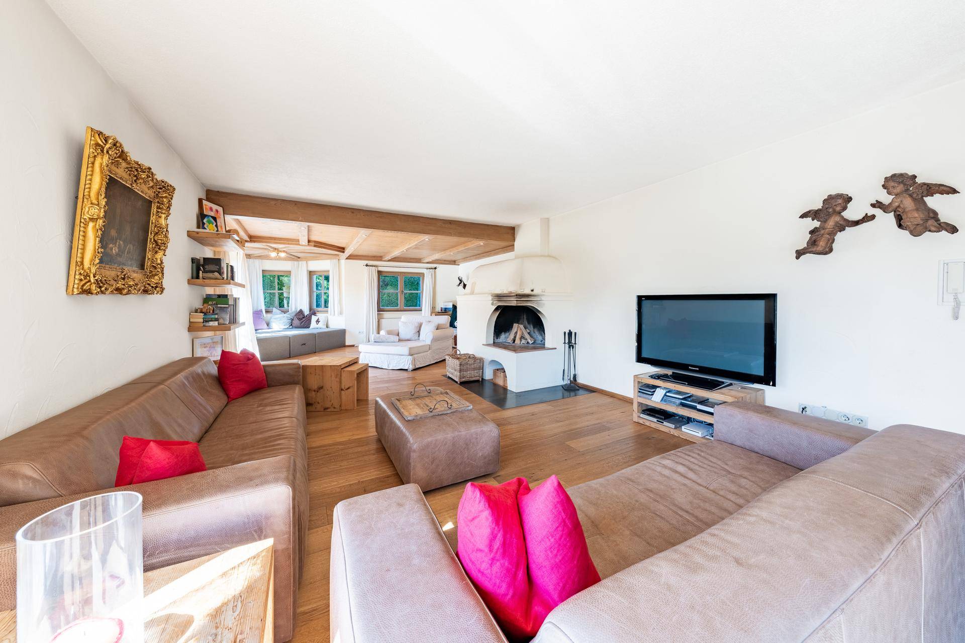 Gemütliches Wohnzimmer mit Holzbalken, Parkettboden, Kamin und bequemen Ledersofas in hellem Ambiente.