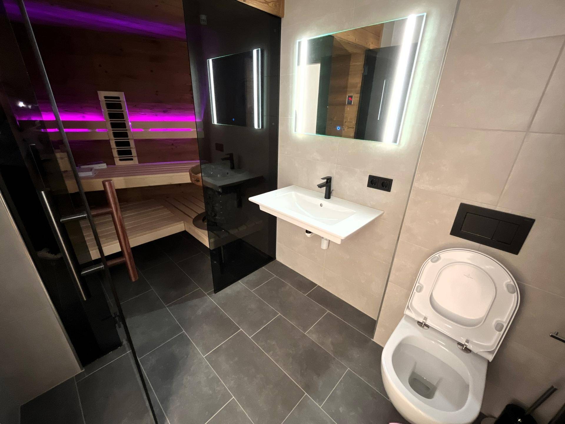 Modernes Badezimmer mit Dusche, WC und integrierter Sauna mit stimmungsvoller Beleuchtung.