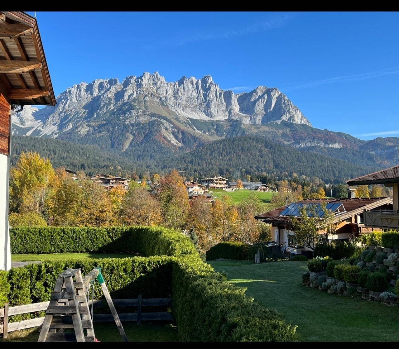 Gepflegter Gartenbereich mit Hecken und Spielgerät, umgeben von einer beeindruckenden Bergkulisse.