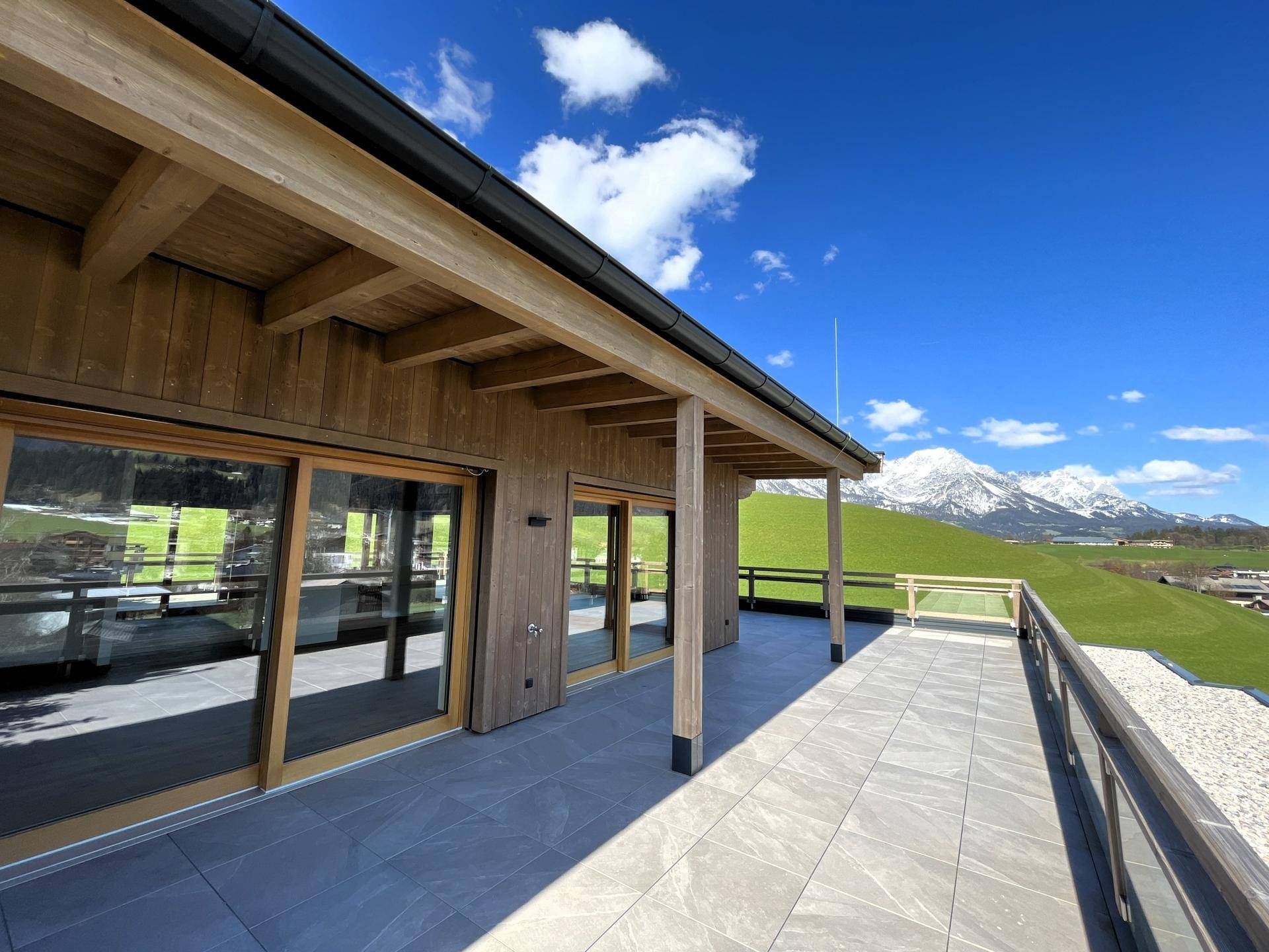 Weitläufige Terrasse mit Bergblick, Fliesenboden und Holzverkleidung unter blauem Himmel.