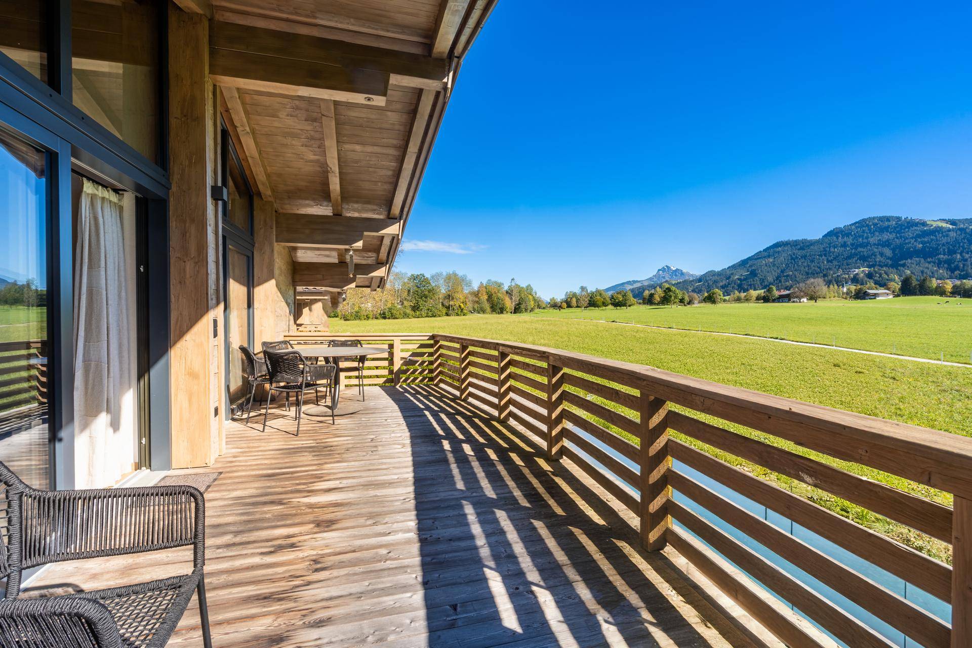 Langer Holzbalkon mit Panoramablick auf die umliegende Berglandschaft und weite Felder.