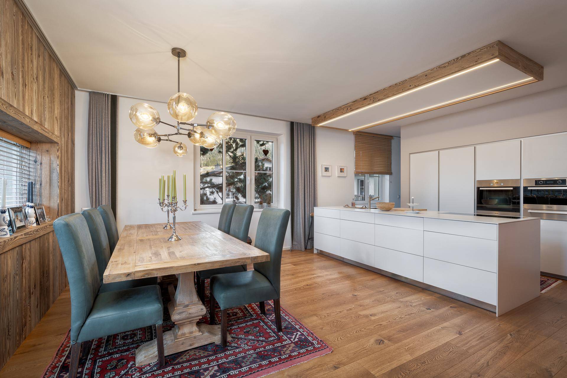 Offener Wohn-Essbereich mit moderner Küche, Holztisch und Holzwandverkleidung, ideal für gesellige Abende.