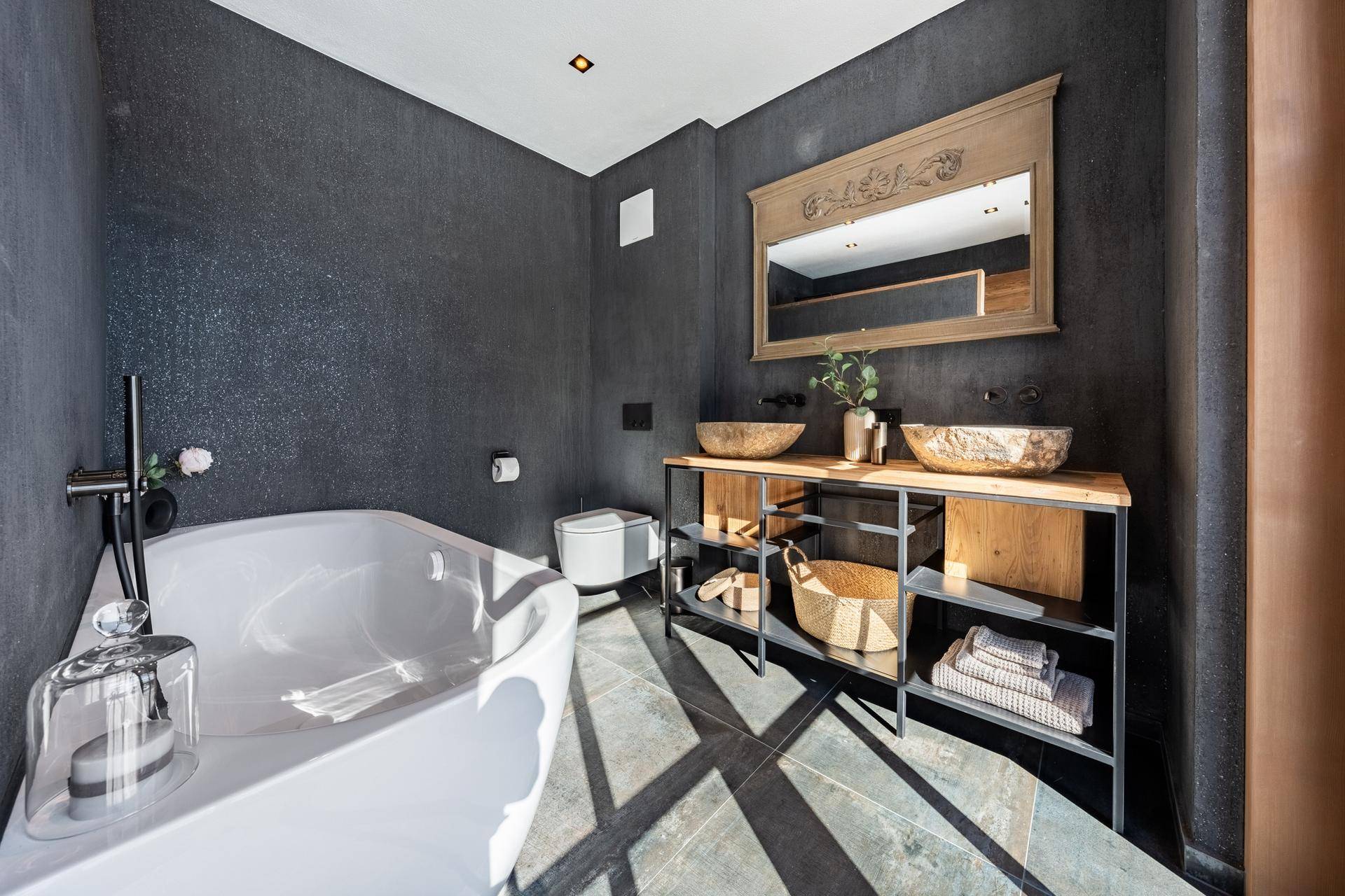 Stilvolles Badezimmer mit freistehender Badewanne, Doppelwaschbecken und dunklen Wänden.