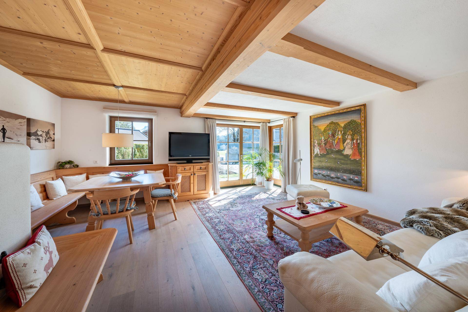 Gemütlicher Wohn- und Essbereich im Landhausstil mit Holzbalkendecke und Zugang zum Garten.