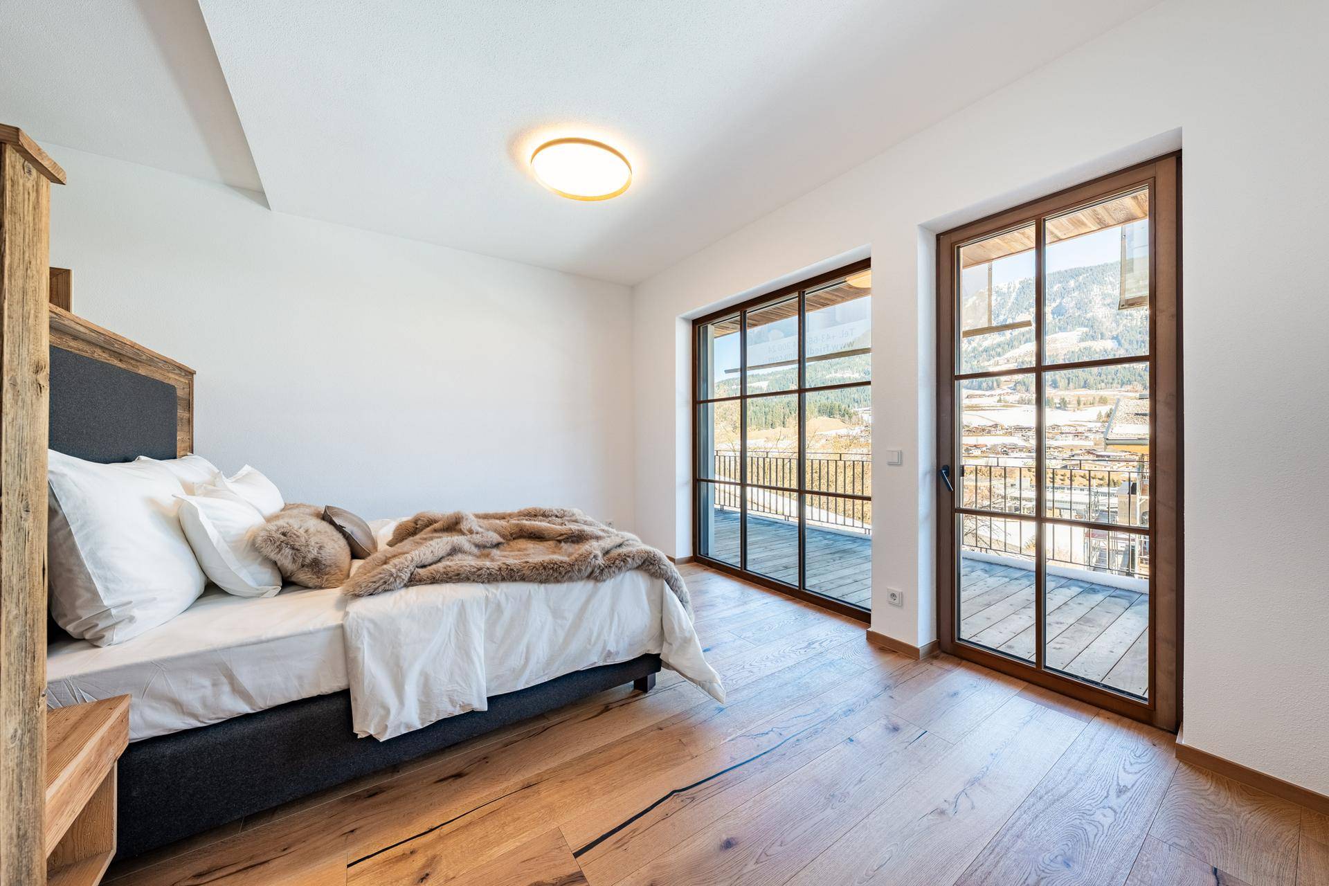 Helles Schlafzimmer mit Holzboden, großen Fenstern und Zugang zum Balkon mit Bergblick.
