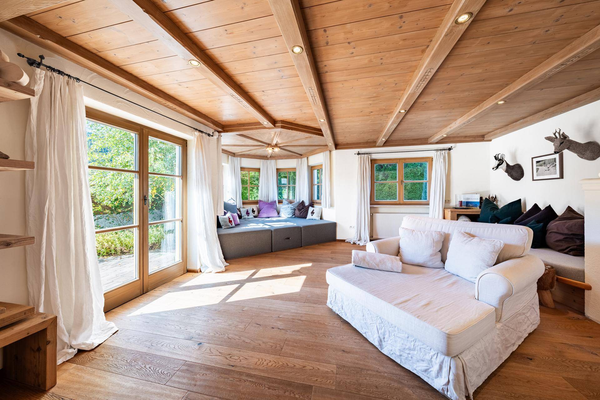 Heller Wohnbereich mit Holzbalkendecke, großen Fenstern und einer gemütlichen Sitzbank am Fenster mit Gartenblick.