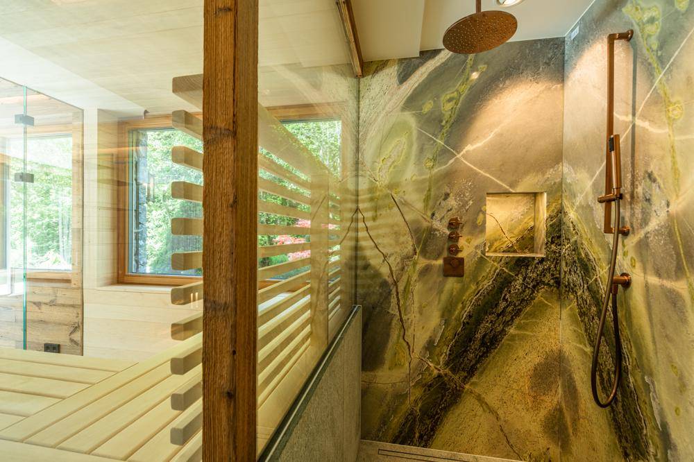 Moderne Dusche mit auffälligen Natursteinwänden und Regenduschkopf in einem luxuriösen Bad.