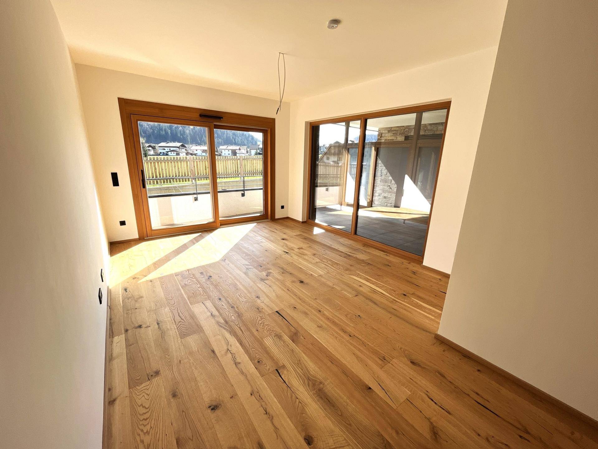 Heller Raum mit Holzboden und großen Schiebetüren, die viel Sonnenlicht hereinlassen und Zugang zum Balkon bieten.
