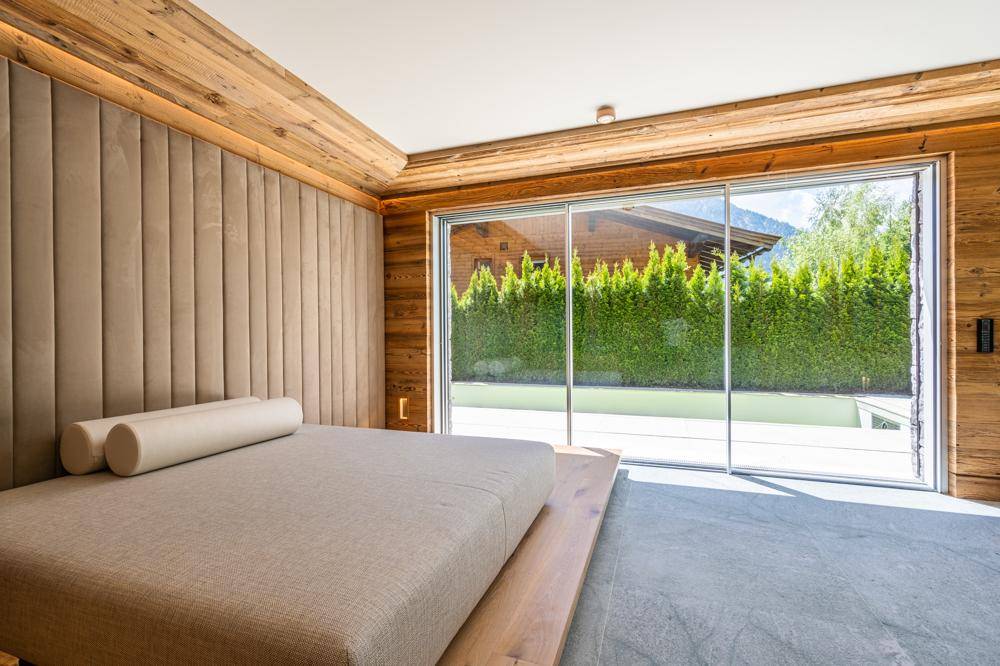 Schlafzimmer mit Holzwänden, gepolstertem Kopfteil und großen Schiebetüren zum Garten.