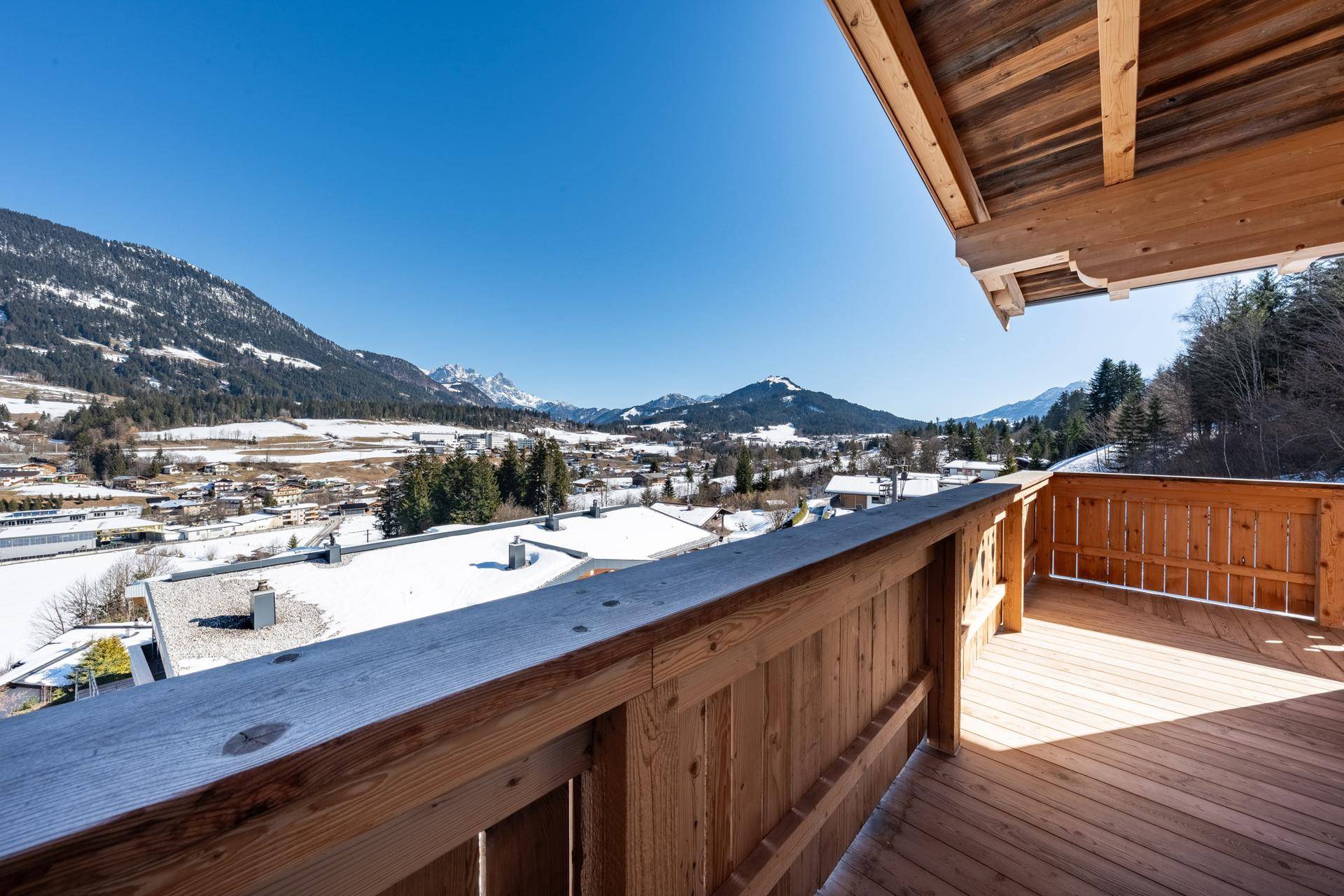 Sonniger Holzbalkon mit weitem Panoramablick auf die verschneite Berglandschaft und das Tal.