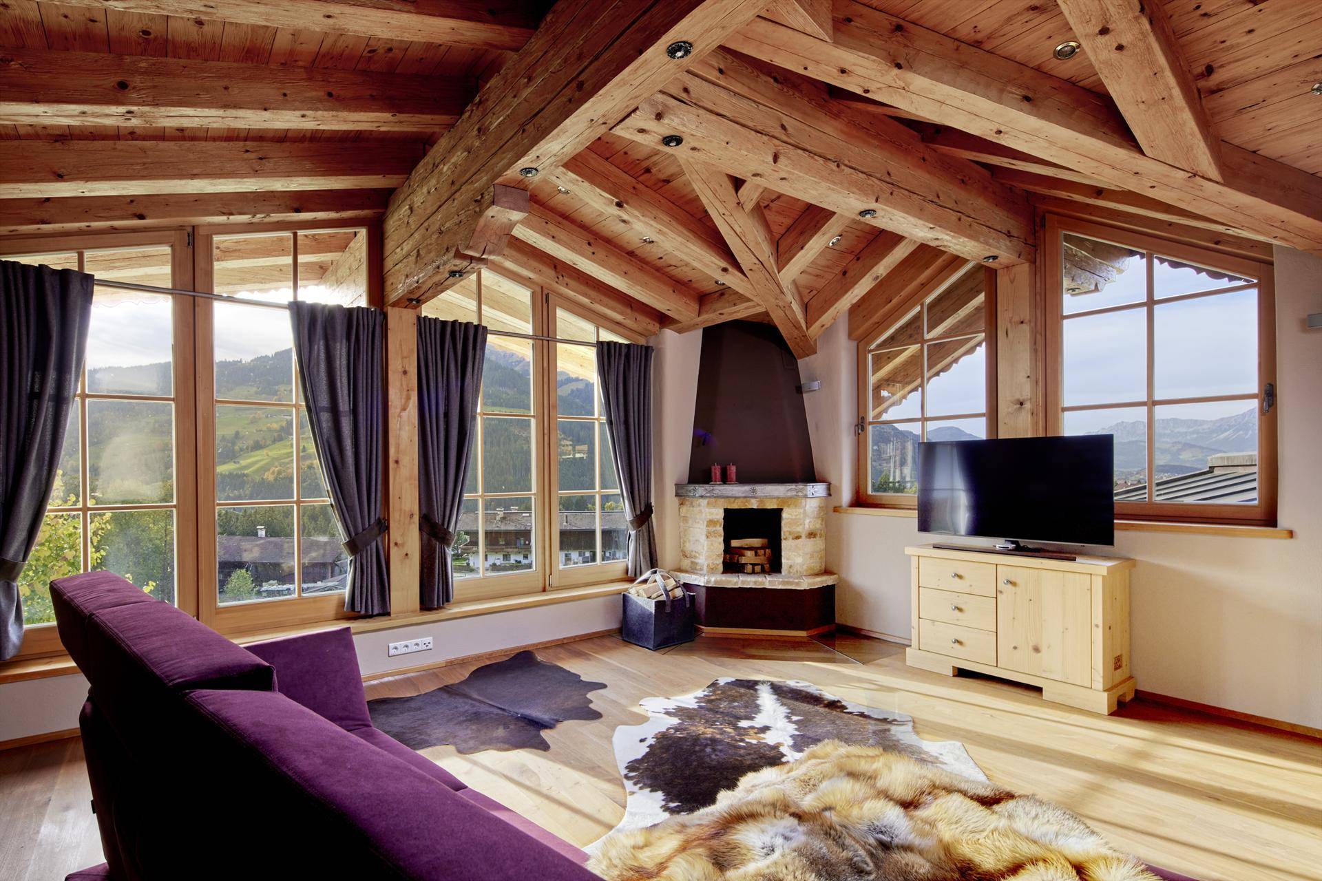 Gemütliches Wohnzimmer im Dachgeschoss mit Holzbalken, Kamin und großen Fenstern mit Bergblick.
