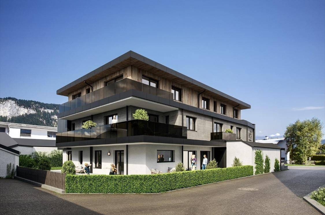 Neubau-Wohngebäude mit modernen Balkonen, großen Fenstern und gepflegter Hecke in alpiner Umgebung.