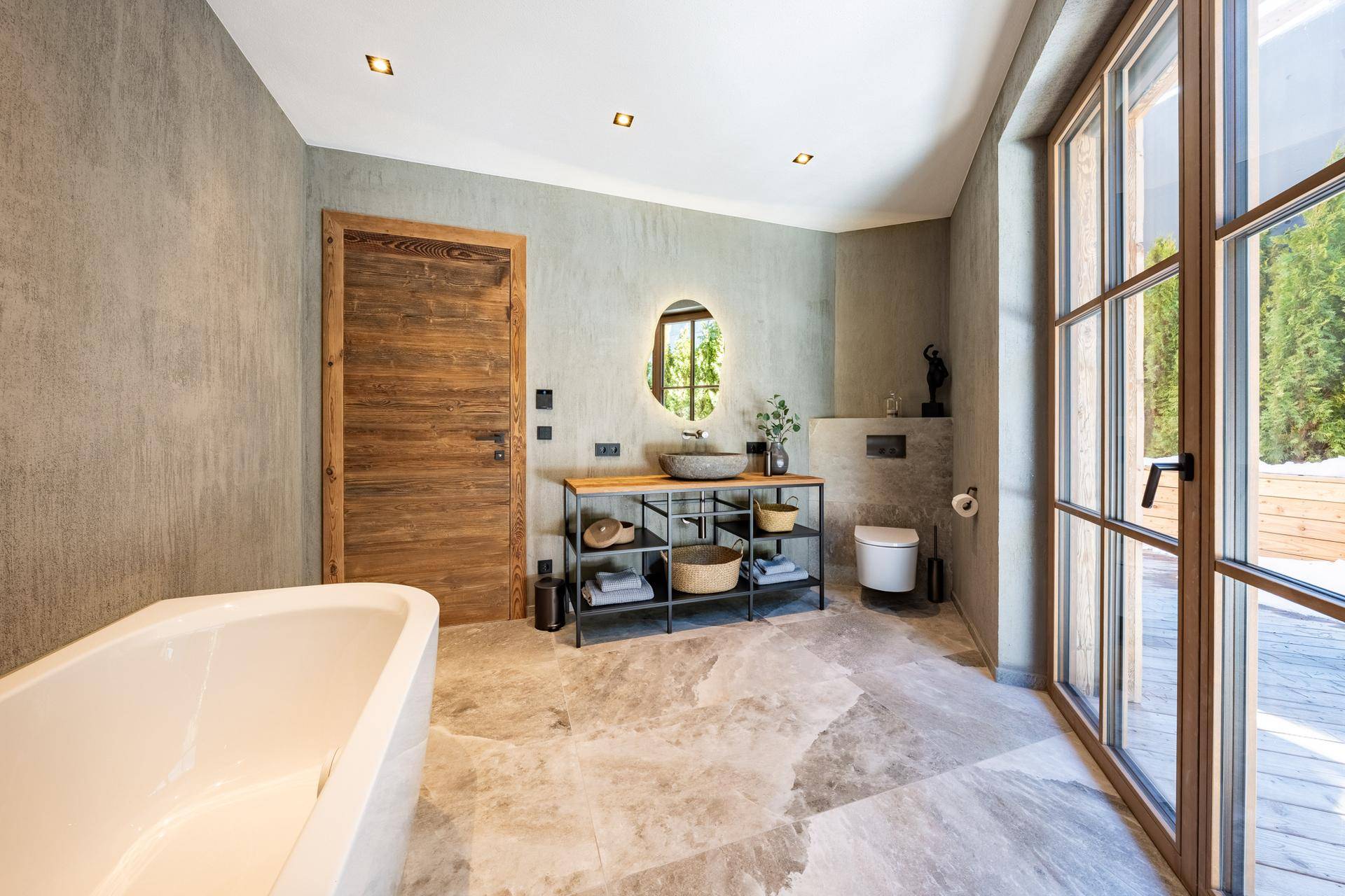Modernes Badezimmer mit freistehender Badewanne, Steinwaschbecken und Zugang zur Terrasse.
