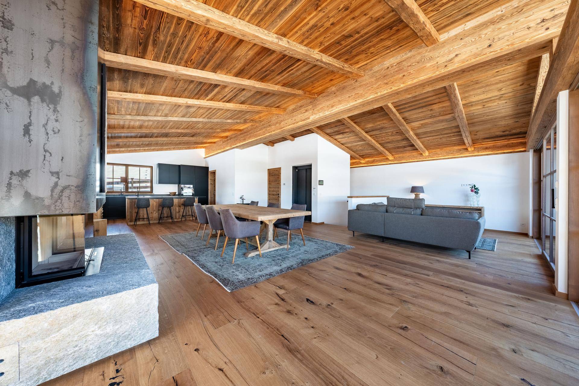 Geräumiger offener Wohnbereich mit Kamin, Holzboden und Blick auf die moderne Küche.