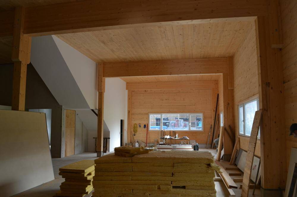 Großer Innenraum im Bau mit Holzbalken, Holzverkleidung und gestapeltem Dämmmaterial.