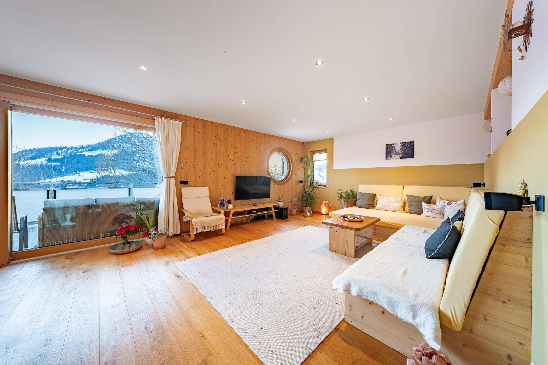 Geräumiges Wohnzimmer mit Holzboden, großen Fenstern und Panoramablick auf die Berge.