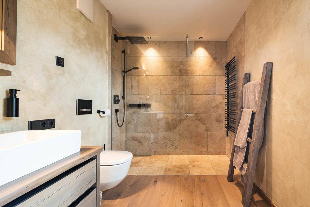 Elegantes Badezimmer mit begehbarer Dusche, Natursteinfliesen und beheiztem Handtuchhalter.