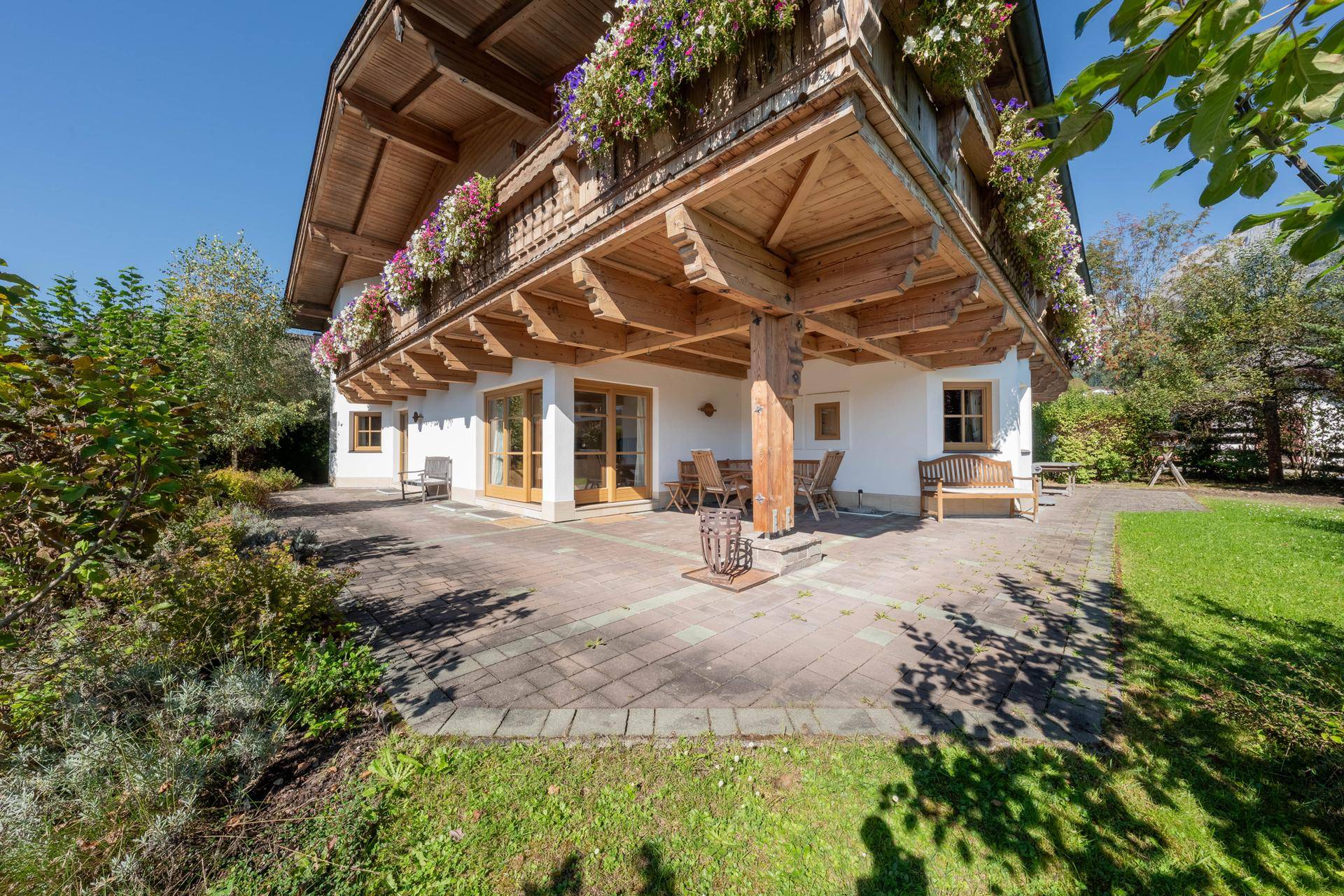Sonniger Terrassenbereich mit Sitzgelegenheiten und Zugang zum Garten, umgeben von üppigem Grün.