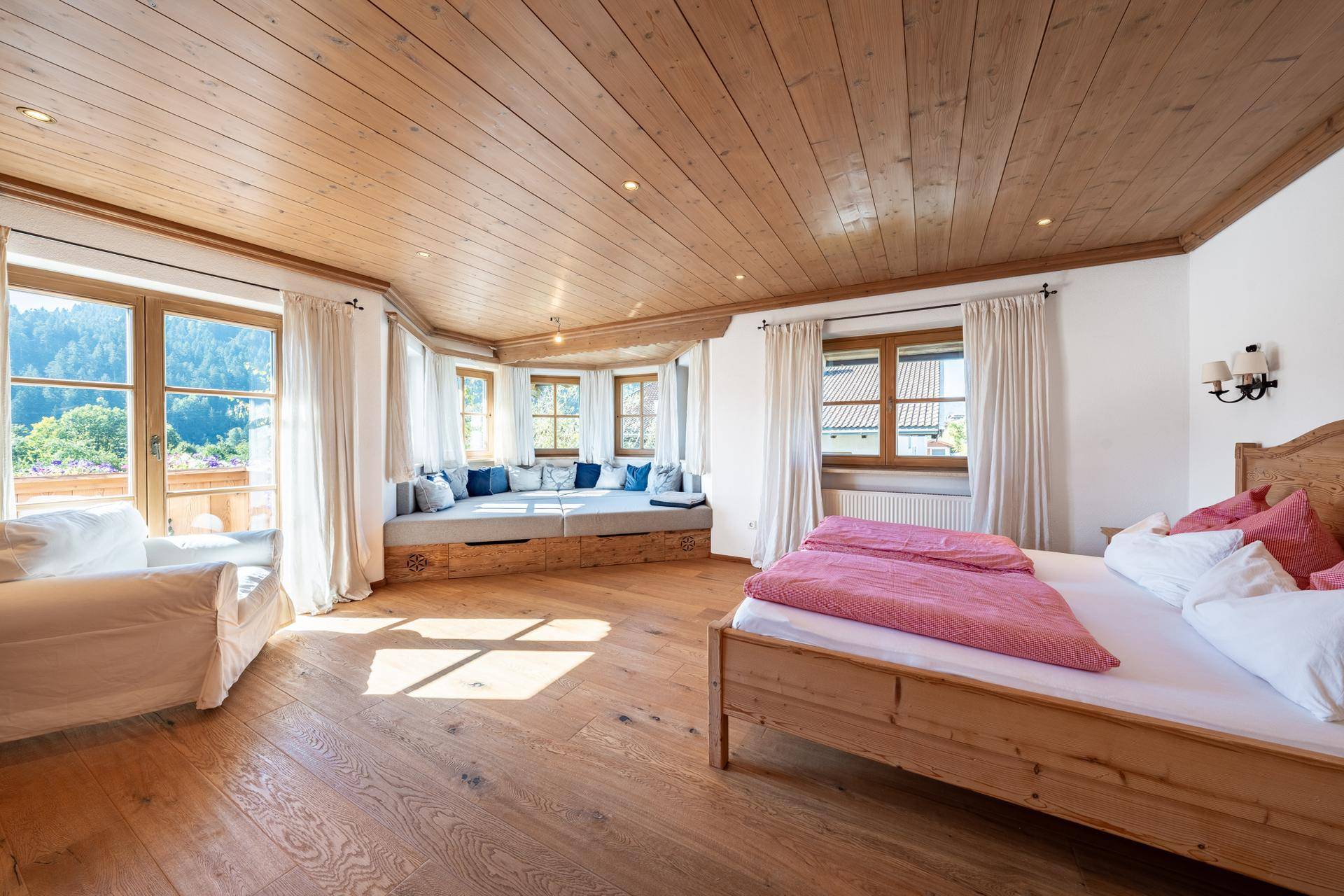 Helles Schlafzimmer mit Holzboden, Holzbalkendecke und einer gemütlichen Fenstersitzbank mit Balkonzugang.