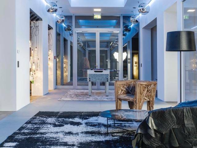 Heller Flur mit modernen Leuchten, einem Kickertisch und einem einzigartigen Holzstuhl.