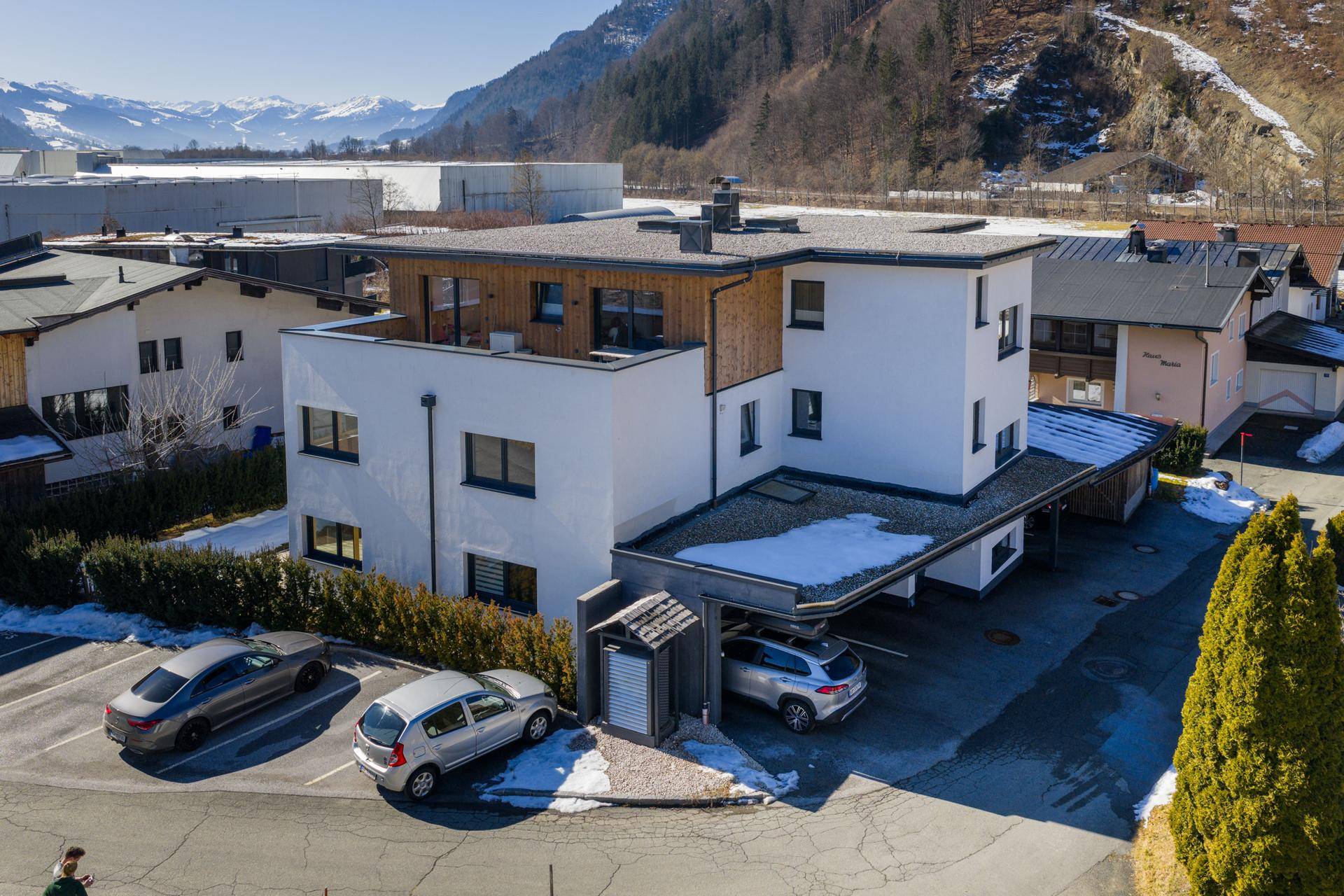 Ansicht der modernen Wohnanlage mit Carport und Parkplätzen in einer bergigen Umgebung.