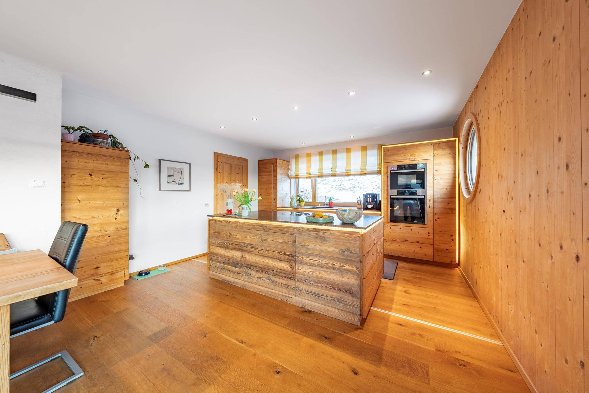 Moderne Holzküche mit Kochinsel, integrierten Geräten und runden Fenstern.