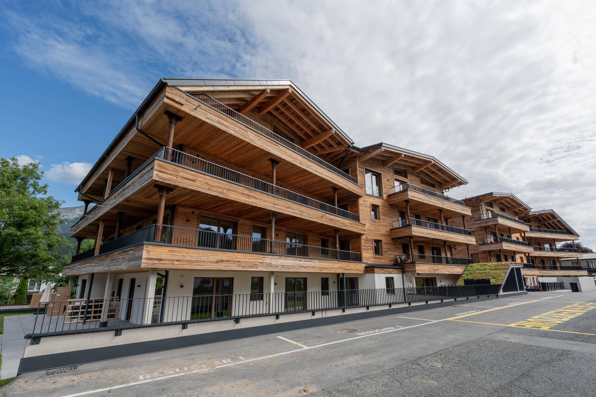 Modernes Apartmenthaus mit Holzfassade und großzügigen Balkonen, umgeben von einer gepflegten Außenanlage.