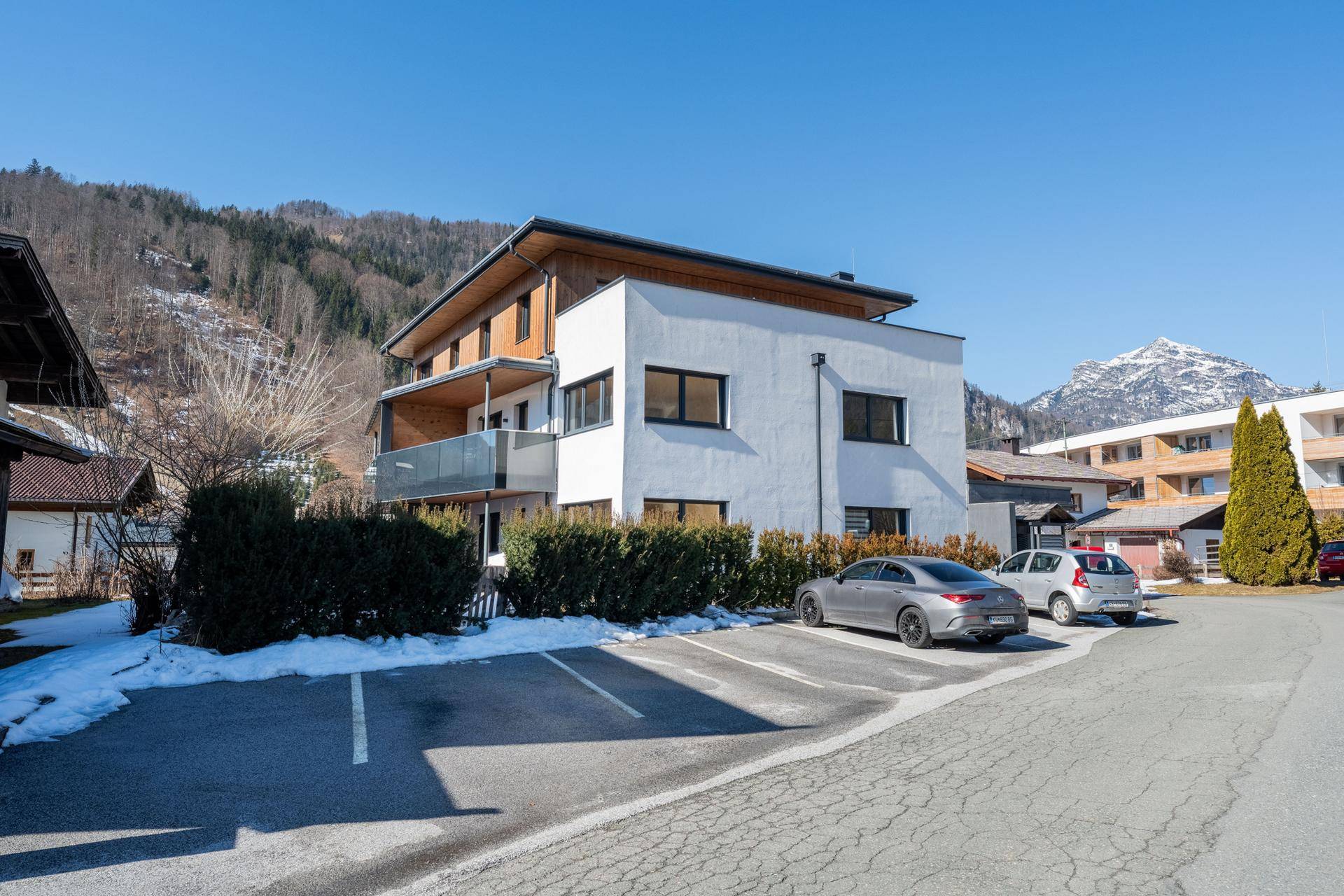 Moderne Wohnanlage mit weißer Fassade und Holzdetails, umgeben von Hecken und Parkplätzen.
