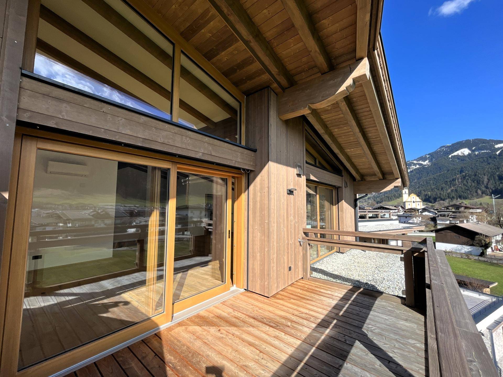 Sonniger Holzbalkon mit Bergblick und großen Schiebetüren zum Innenbereich.