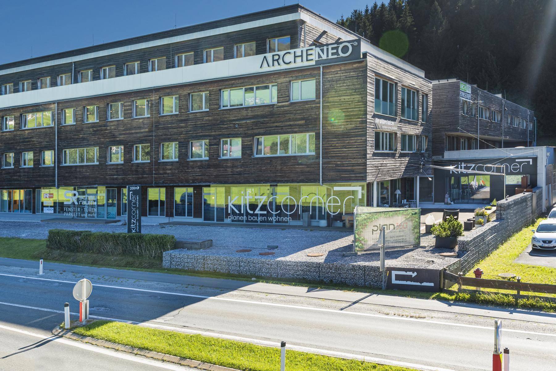Modernes Geschäftsgebäude mit Holzfassade und großen Fenstern in einer grünen Umgebung.
