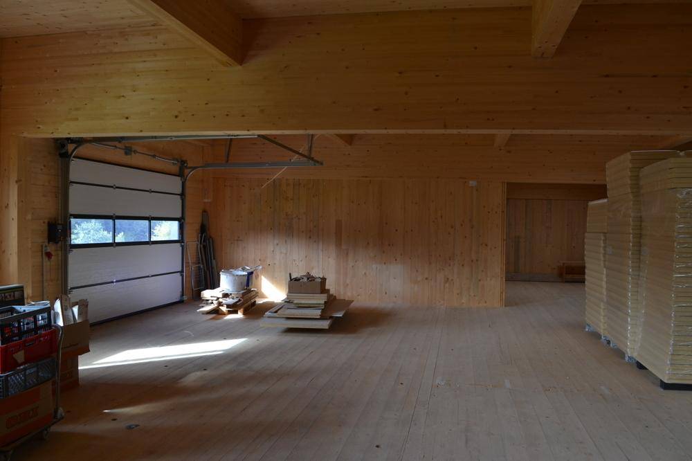 Geräumiger Lagerraum mit Holzverkleidung, Holzbalken, einem Rolltor und gestapeltem Dämmmaterial.