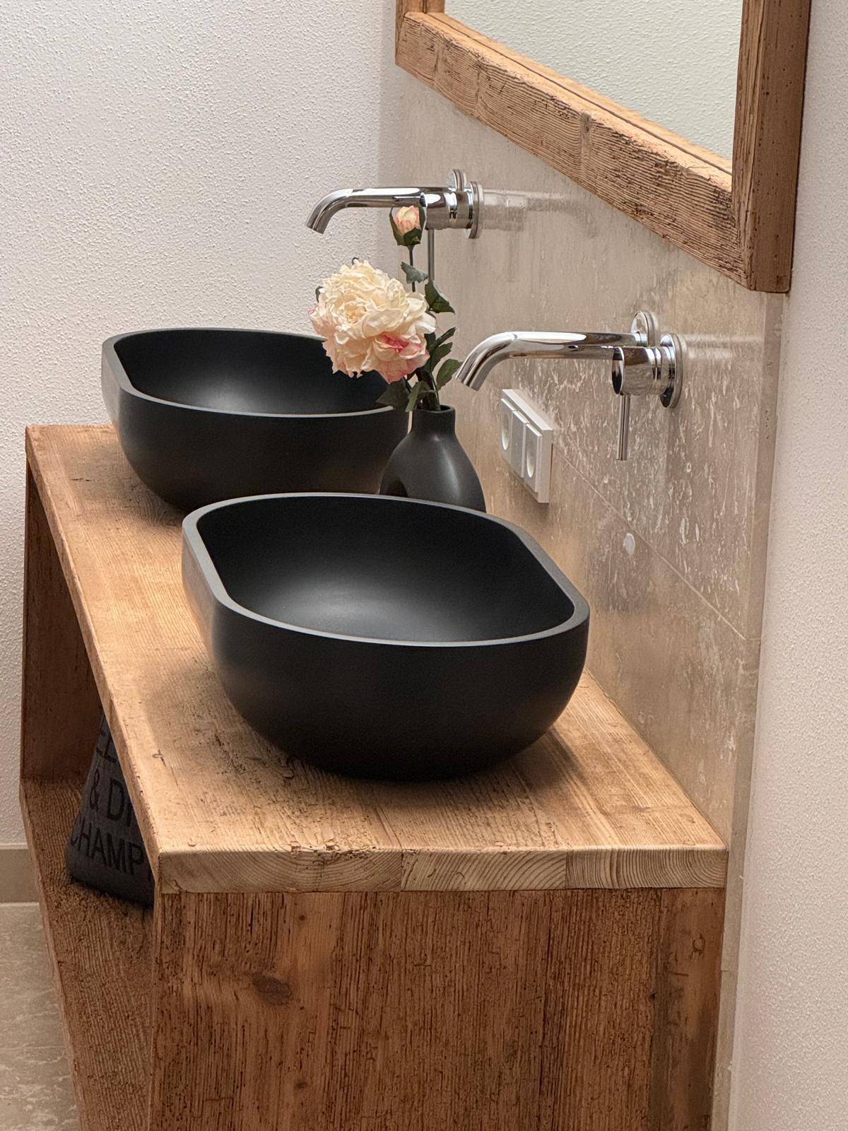 Elegantes Badezimmer mit zwei schwarzen Natursteinwaschbecken und rustikalem Holzwaschtisch.