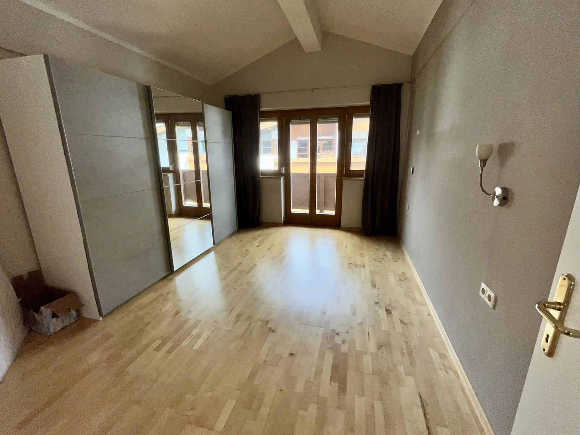 Schlafzimmer mit Holzboden, Spiegelschrank und Zugang zu einem französischen Balkon oder einer Terrasse.